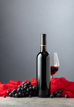 Bottle of red wine with grapes on a grey background.