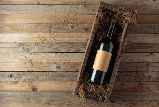 Bottle of red wine with empty label in an antique wooden box with hay.