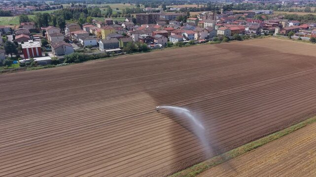 Aerial drone view of a large gun sprinkler watering newly planted vegetable crops in an agricultural field in Mediglia, Lombardy, Italy.