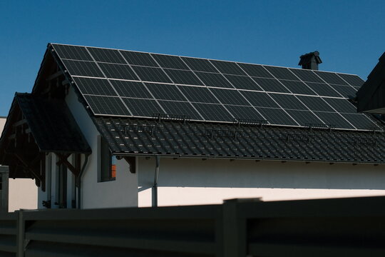 Large rooftop solar panel array installed on a modern residential house under clear blue sky, representing renewable electricity, energy independence and sustainable living.