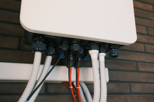Hybrid energy inverter with battery, grid and load connections mounted on a brick wall, illustrating residential solar power, backup electricity and home energy storage.