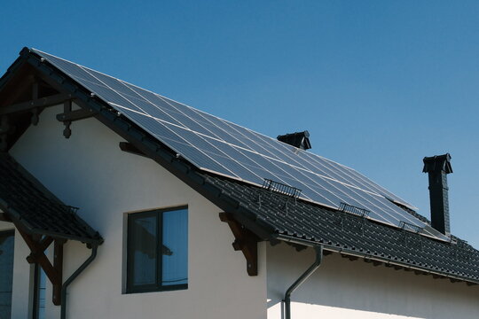 Large rooftop solar panel system on a modern residential house under clear blue sky, illustrating renewable electricity, energy independence and sustainable home power.