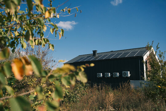 Modern house with rooftop solar panels under blue sky, surrounded by natural vegetation, representing renewable energy, energy independence and autonomous living.