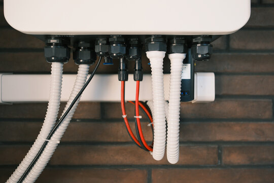 Close-up of electrical connections and wiring beneath a residential solar inverter, showing battery, grid and load cables in a modern home energy storage installation.