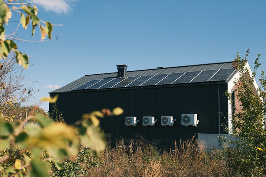 Modern house with rooftop solar panels and outdoor heat pump units under clear blue sky, representing renewable energy, self-sufficiency and sustainable home technology.