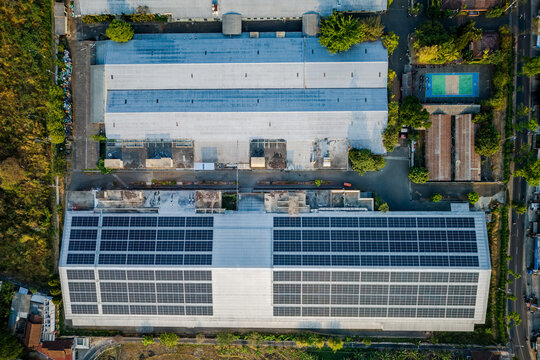 Aerial view of a large industrial factory building featuring extensive rooftop solar panel arrays, surrounded by green vegetation and nearby structures in Semarang Regency, Central Java, Indonesia.