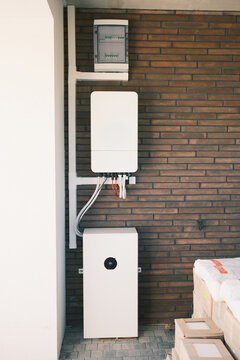Residential solar energy storage system with wall mounted inverter, electrical distribution panel and home battery installed against a brick wall for backup power.