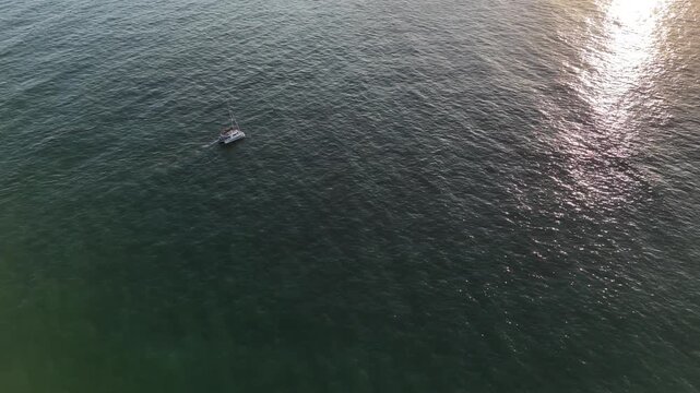 Aerial view of white sailboat on deep blue ocean water creating foamy waves. Nautical vessel sails on calm sea surface, journey towards horizon, exploring vast oceanic expanse. 