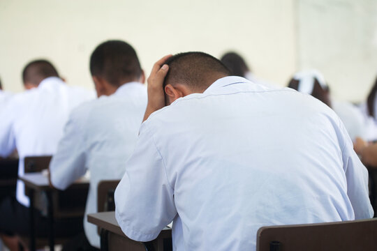 Stressed Male Student Holding Head During Final Examination in Classroom