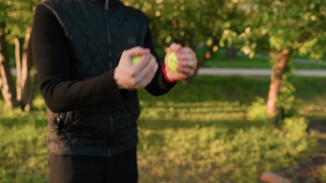Close up view shows two people exchanging bright green tennis balls. One person wearing checkered coat holds initial handover while another person reaches out to receive it in outdoor park