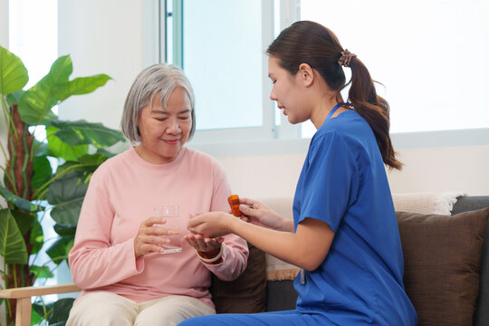 Asian caregiver assisting senior woman with medication at home for healthcare
