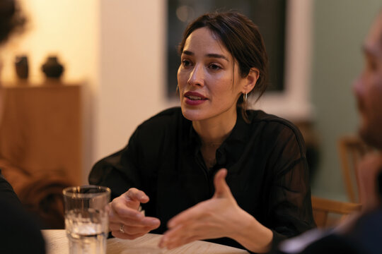 A woman animatedly discussing ideas in a cozy, stylish indoor setting with a glass of water nearby, highlighting interpersonal communication and connection among people.