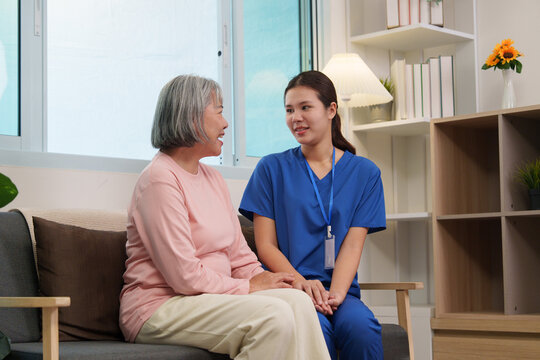 Asian caregiver sitting on sofa comforting senior woman during home health visit