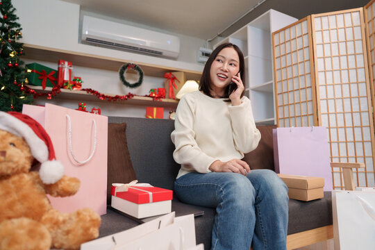 Asian woman talking on smartphone surrounded by Christmas gifts at home