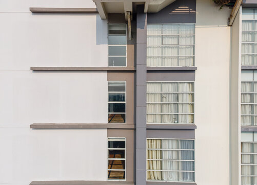 Aerial view of a modern building facade featuring clean white and grey walls, large windows with white curtains, and horizontal architectural lines in Purwokerto, Central Java, Indonesia.