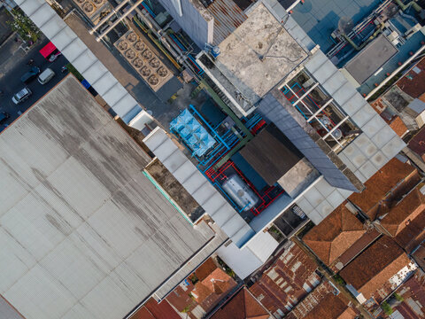 Aerial view of a building rooftop featuring industrial HVAC units, cooling towers, and ventilation systems surrounded by urban residential rooftops in Purwokerto, Central Java, Indonesia.