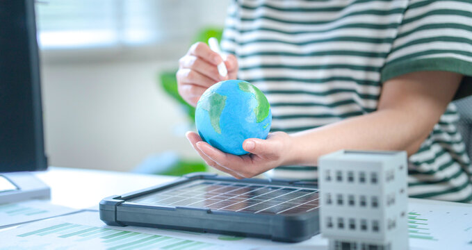 An ESG designer holds a globe, symbolizing an environmentally conscious business approach that incorporates clean energy, solar power, energy-efficient buildings, and digital-age energy management sys