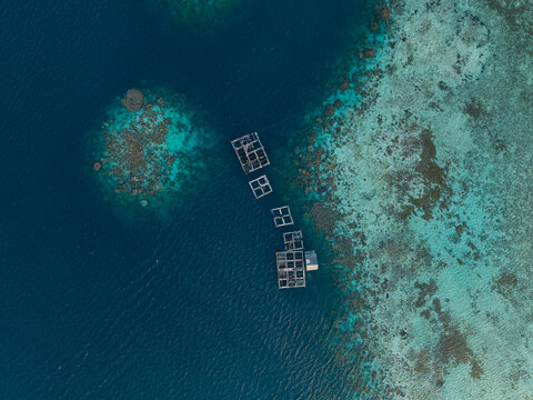 Aerial view of a fish cage floating in the turquoise waters of the ocean near the coral reef in Karimunjawa, Jawa Tengah, Indonesia.