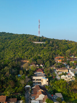 Aerial view of the Karimunjawa sign on a lush green hillside with a tall communication tower, overlooking a residential area, Karimunjawa, Central Java, Indonesia.