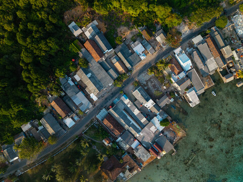 Aerial view of Karimunjawa village showing coastal houses, narrow roads, dense tropical vegetation, and clear turquoise waters in Karimunjawa, Central Java, Indonesia.