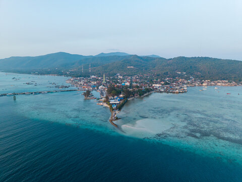 Aerial view of Karimunjawa Town Square surrounded by coastal buildings, turquoise waters, and lush green hills in Karimunjawa, Central Java, Indonesia.