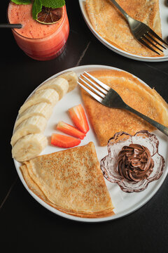 A plate of crepes filled with chocolate spread and topped with banana slices and mint