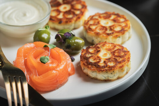 Savory Syrniki with Smoked Salmon, Olives and Sour Cream on White Plate