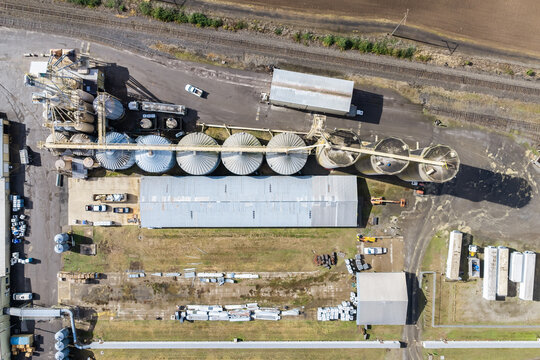 Aerial view of a grain elevator facility with large metal silos, a long warehouse, and adjacent railroad tracks in Woodburn, Oregon, United States.