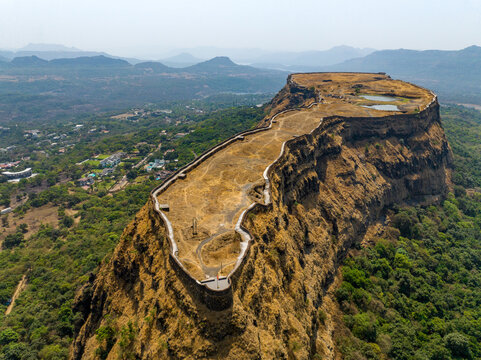 Aerial view of Korigad Fort featuring historic stone fortifications, plateau, and water reservoirs set amidst the lush green landscape in Peth Shahapur, Maharashtra, India.