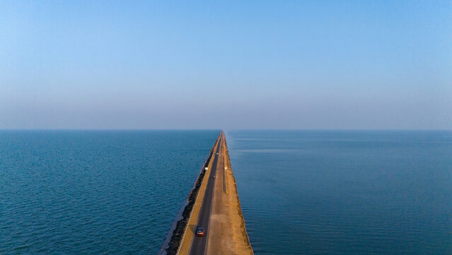 Aerial view of the Road to Heaven stretching across the vast blue waters of the Rann of Kutch, with a single car driving along the narrow asphalt road in Bhuj, Gujarat, India.