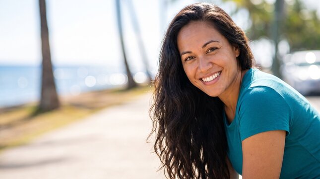 Bright white smile headshot of a beautiful Native Hawaiian woman with wavy hair, happy positive expression, oceanfront path