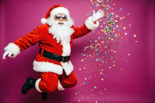 Un alegre Santa Claus, con un traje rojo intenso y gafas de sol de espejo, saltando en el aire en el lado izquierdo de un fondo magenta llamativo