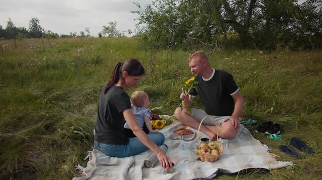 Mother and father having fun with their toddler at picnic. Happy family enjoying time together outdoors