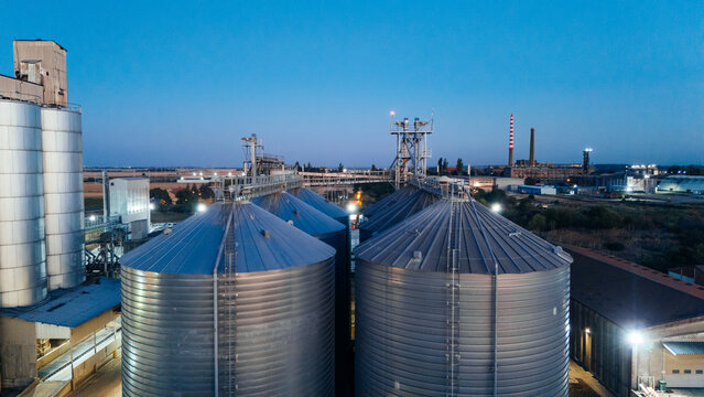 Aerial view of large industrial grain silos at dusk with illuminated metal structures and storage tanks in Sremska Mitrovica, Vojvodina, Serbia.