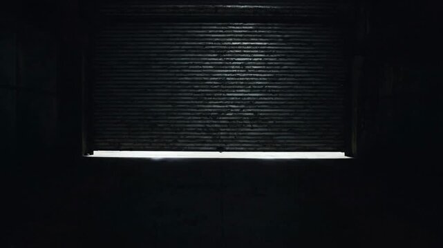 Industrial metal roller shutter closing in dark warehouse facility, automatic garage door descending