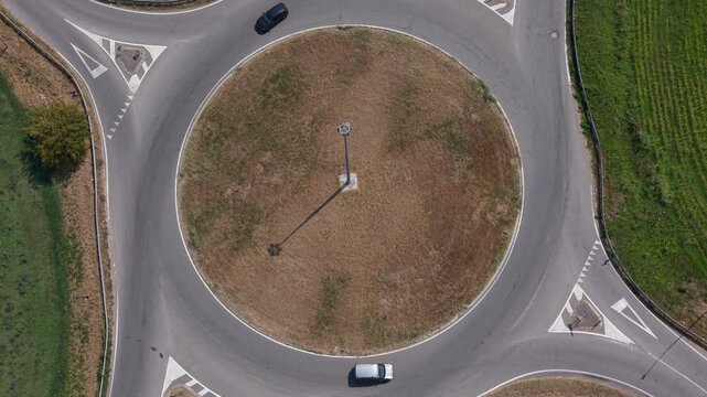 Drone view of a rural roundabout in Mediglia, Italy with a small number of cars moving through the road junction. Suitable for transportation, infrastructure, travel and regional landscape content.