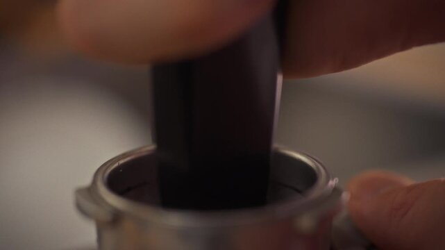 In a lively cafe, a barista uses a coffee press to tamp espresso grounds into the horn, crafting a rich, strong brew that showcases precise technique and the art of coffee preparation