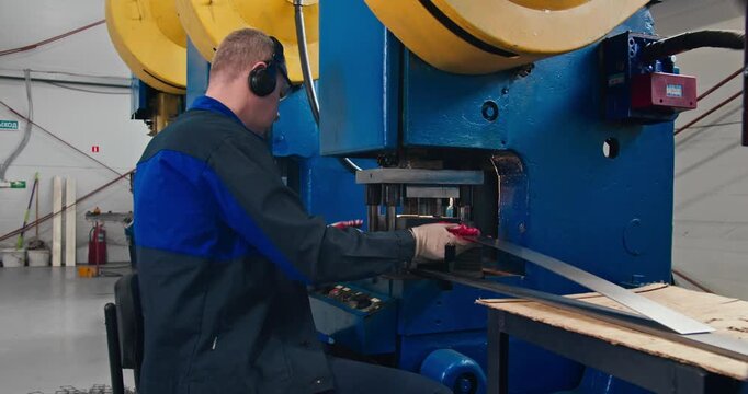 Metal stamping with machine operator at work in industrial workshop. Medium shot blue collar employment in metal parts manufacturing
