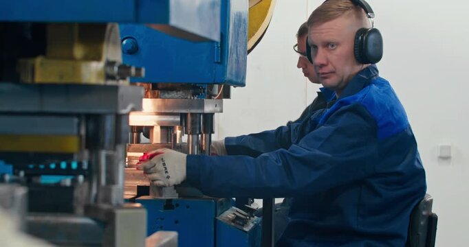 Machine operators at work in metal stamping workshop. Blue collar occupations and industrial component production on mechanical presses, medium shot