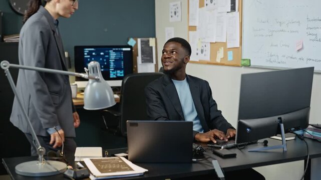 African American young adult programmer typing on computer and discussing cybersecurity data with Caucasian female colleague. Footage suitable for corporate computer and tech business promotions