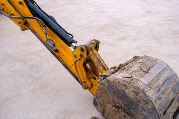 Close-up of a yellow excavator bucket and dirty hydraulic arm resting on a concrete surface. This industrial image is perfect for construction, engineering, heavy machinery, and urban development proj © ismailgazel