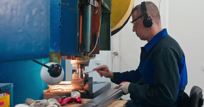 Machine operator bending metal parts in factory workshop. Medium shot of blue collar manufacturing work at mechanical press