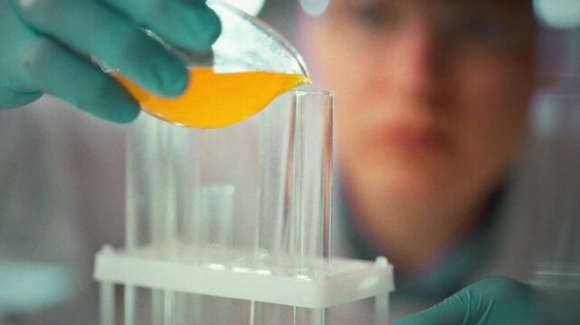 In laboratory, scientist researcher wearing protective gloves carefully pours clear liquid into test tube, starting an experiment. The precise action highlights research methods and safety protocols
