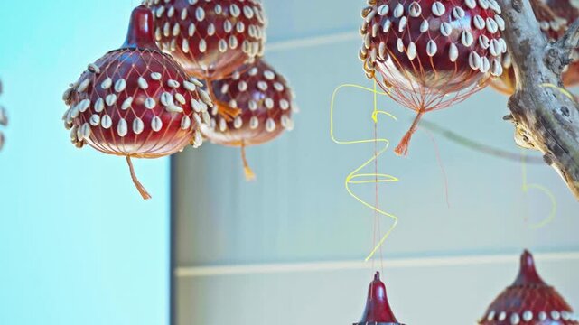 Close-up of traditional handcrafted gourd (calabash) ornaments wrapped in netting and studded with cowrie shells, suspended and gently swaying indoors.