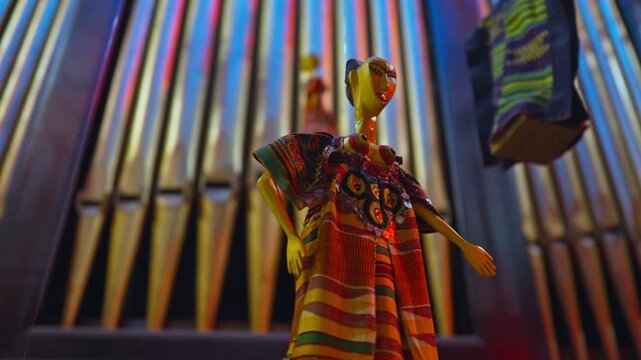 Close-up of an artisan-made figurine dressed in an elaborate, brightly patterned traditional costume with beaded jewelry, displayed for sale at an outdoor market.