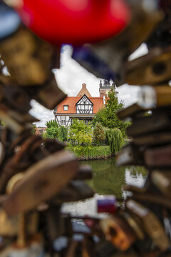 View of a historic half-timbered building with a red roof reflected in the canal, framed by blurred love padlocks on a bridge in Gdansk, Pomeranian Voivodeship, Poland.