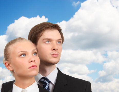 Young business woman and businessman look upward, sky with clouds, collage - Young business couple looks upward against a blue sky. Clouds drift behind them in soft white masses