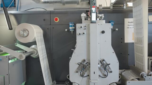 Industrial label converting machine feeds printed barcode labels through rollers and automated finishing equipment during high-speed production in a modern manufacturing facility.