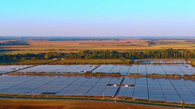 Extensive solar panel installation in agricultural area. Wide aerial shot presents vast rows of solar panels positioned on flat ground near farmland.