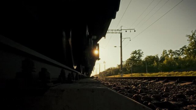 A freight train passes over rails and sleepers close-up on a sunny day in a field location. The concept of rail freight transportation and modern transport logistics